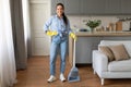 Happy woman standing with broom and dustpan in home interior
