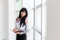 Happy woman standing near the window, writing in a notebook, looking at the camera smiling Royalty Free Stock Photo