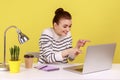 Happy woman in striped shirt pointing to laptop screen and sincerely laughing talking on video call. Royalty Free Stock Photo