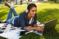 Happy woman student lies outdoors in a park using laptop computer listening music. Royalty Free Stock Photo