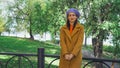 happy woman in stylish beret and coat standing near fence in park. Royalty Free Stock Photo