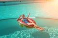 Happy woman in a swimsuit and sunglasses floating on an inflatable ring in the form of a watermelon, in the pool during