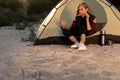 Happy woman in tent eating sausage fried on campfire while resting in camp. having a picnic at the campsite on the beach Royalty Free Stock Photo