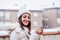 Happy woman on terrace at home enjoying cup of hot coffee, neighborhood background. Snow in the city Royalty Free Stock Photo