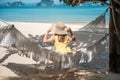 Happy Woman Traveler is relaxing in a hammock on the paradise beach. Female tourist in yellow dress rest near tropical sea. Royalty Free Stock Photo