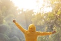 Happy woman traveler in yellow sweater with hood is standing with raised arms Royalty Free Stock Photo