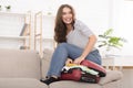 Happy woman trying to close suitcase, preparing for vacation