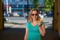 A happy woman in a turquoise dress stands in the yard and eats a waffle cone on a warm summer day. Beautiful blonde in sunglasses Royalty Free Stock Photo