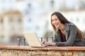 Happy woman using a laptop and looking at you in a balcony Royalty Free Stock Photo