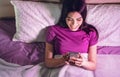 Happy woman using mobile smartphone in bed - Young girl having fun on social media networks at home Royalty Free Stock Photo