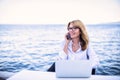 Happy woman using phone and laptop while sitting at the seaside Royalty Free Stock Photo