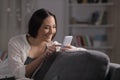 Happy woman using phone in the night on a couch