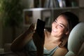 Happy woman using phone at night with lightened face