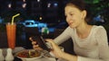 Happy woman using smartphone and messaging sitting in restaurant at night Royalty Free Stock Photo