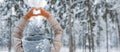 woman mittens dressed fashionable gray stands with her back makes heart gesture with her hands against background snowy