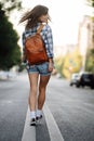 Happy woman walking on the road, wearing brown leather backpack