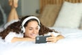 Happy woman watching videos on smart phone on a bed Royalty Free Stock Photo