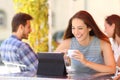 Happy woman watching videos in a tablet in a coffee shop