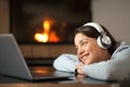 Happy woman wathing media on laptop near a fireplace