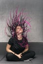 Happy woman waves her dreads with long violet dreadlocks sitting on sofa. Vertical frame. Stylish girl