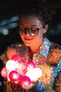 Happy woman wearing glowing jacket with sequins is holding light balls in her hands