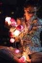 Happy woman wearing glowing jacket with sequins is holding light balls in her hands