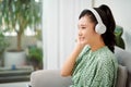 Happy woman wearing wireless headphones listening to music sitting on a couch in the living room at home Royalty Free Stock Photo