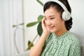 Happy woman wearing wireless headphones listening to music sitting on a couch in the living room at home Royalty Free Stock Photo