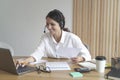 Happy woman wears headphones while sits at desk at home office looks at laptop screen works online Royalty Free Stock Photo