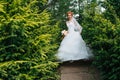 Happy woman in wedding dress walking through junipers in a park Royalty Free Stock Photo