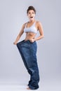 Happy woman wearing jeans after weight-loss on gray background