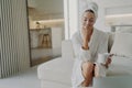 Happy woman in white bathrobe drinking tea and relaxing on sofa after taking shower or bath Royalty Free Stock Photo