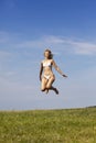 The happy woman in white bikini jumps in a summer green field against the blue sky Royalty Free Stock Photo