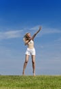 The happy woman in white bikini and shorts jumps in a summer green field against the blue sky Royalty Free Stock Photo