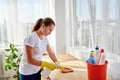 Happy woman in white shirt and yellow protective rubber gloves cleaning at home and wiping dust on wood tablel with spray. Royalty Free Stock Photo