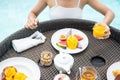 Happy woman in white swimsuit having Floating Breakfast tray in luxury pool hotel, young female with enjoy in tropical resort. Royalty Free Stock Photo