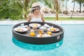 Happy woman in white swimsuit having Floating Breakfast tray in luxury pool hotel, young female with sunglasses enjoy in tropical Royalty Free Stock Photo