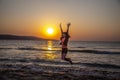 A happy woman who is jumping on the beach in sunrise on beautiful background with sea and sun shining on water Royalty Free Stock Photo