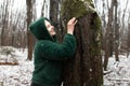 Happy woman in winter forest. Female portrait in snow park. Smiling woman in eco fur jacket touch with hand tree trunk. Royalty Free Stock Photo