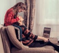 Happy woman working at home on computer and cute kid play with mother. Sitting on sofa, daughter covering mother the eyes with Royalty Free Stock Photo