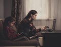 Happy woman working at home on computer and cute kid studing in mobile phone. Family sitting on sofa together near each other. Royalty Free Stock Photo