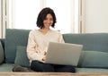 Happy woman working on laptop surfing on the internet and social media sitting on sofa at home Royalty Free Stock Photo