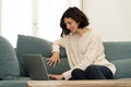 Happy woman working on laptop surfing on the internet and social media sitting on sofa at home Royalty Free Stock Photo