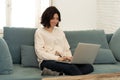 Happy woman working on laptop surfing on the internet and social media sitting on sofa at home Royalty Free Stock Photo