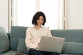 Happy woman working on laptop surfing on the internet and social media sitting on sofa at home Royalty Free Stock Photo