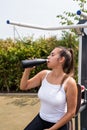 Happy woman working out on the sports ground in sunny summer day, drinking water from the bottle Royalty Free Stock Photo