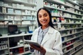 Happy woman working in pharmacy using digital tablet wearing labcoat looking at camera