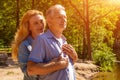 A happy woman embraces a man behind her back, standing on the shore of the lake, in the rays of the sun at sunset Royalty Free Stock Photo