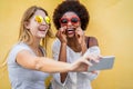 Happy women friends taking selfie standing over yellow wall - Trendy girls with fashion sunglasses having fun laughing together -