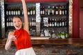 Mid adult woman raising arm holding shot glass among liquor bottles at bar counter, copy space Royalty Free Stock Photo